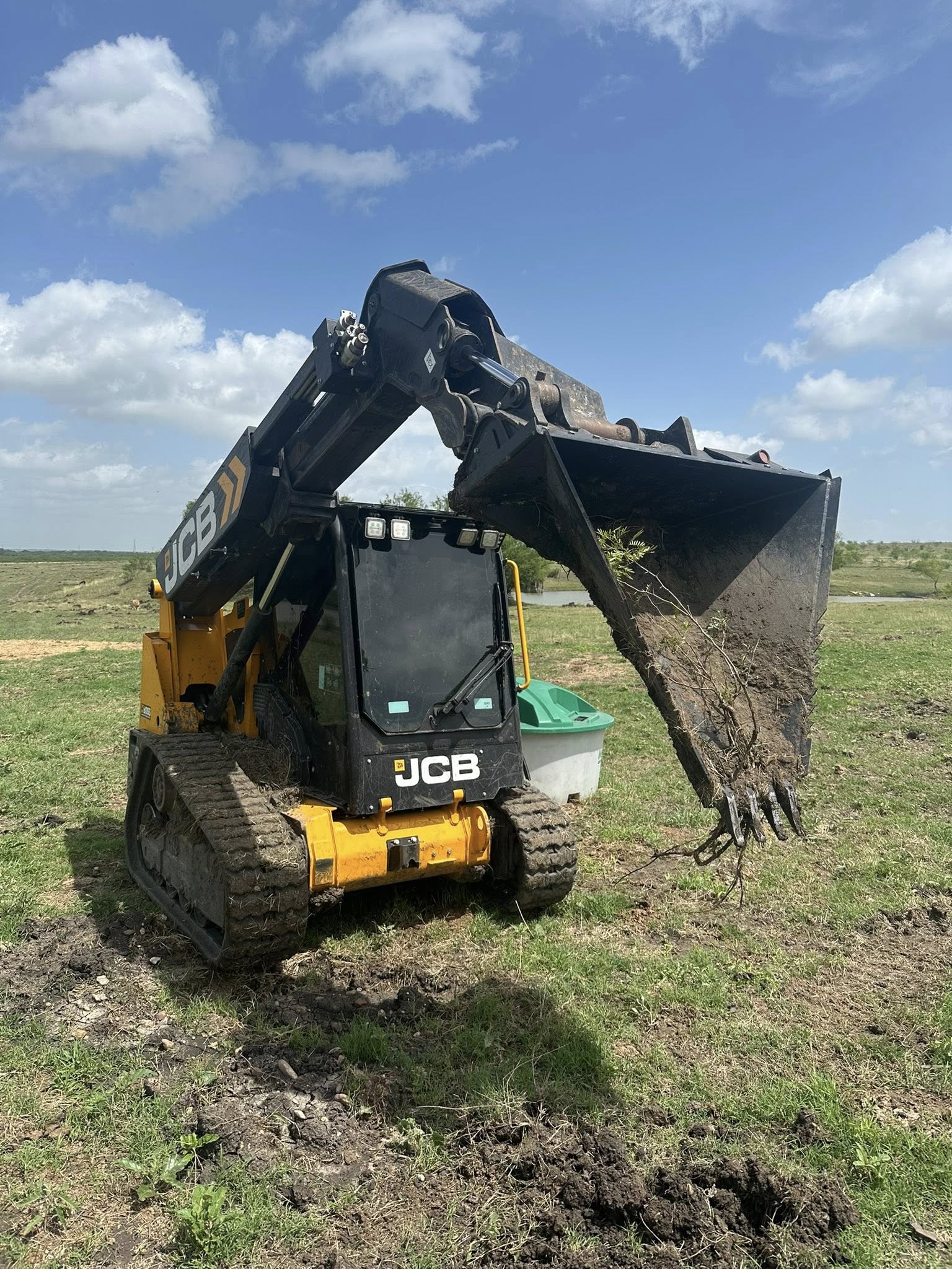 JCB track loader scooping dark soil in open field